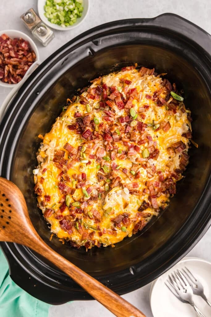 Cooked hash brown casserole topped with bacon and scallions in a slow cooker.