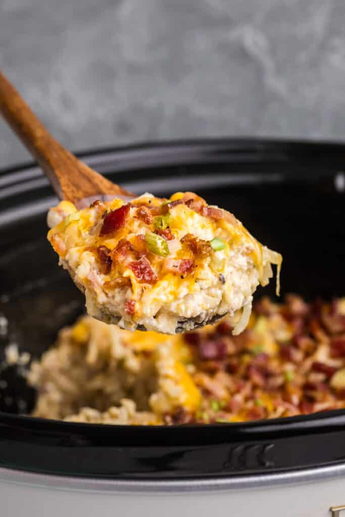 A wooden spoon lifting a portion of cheesy hash brown casserole.