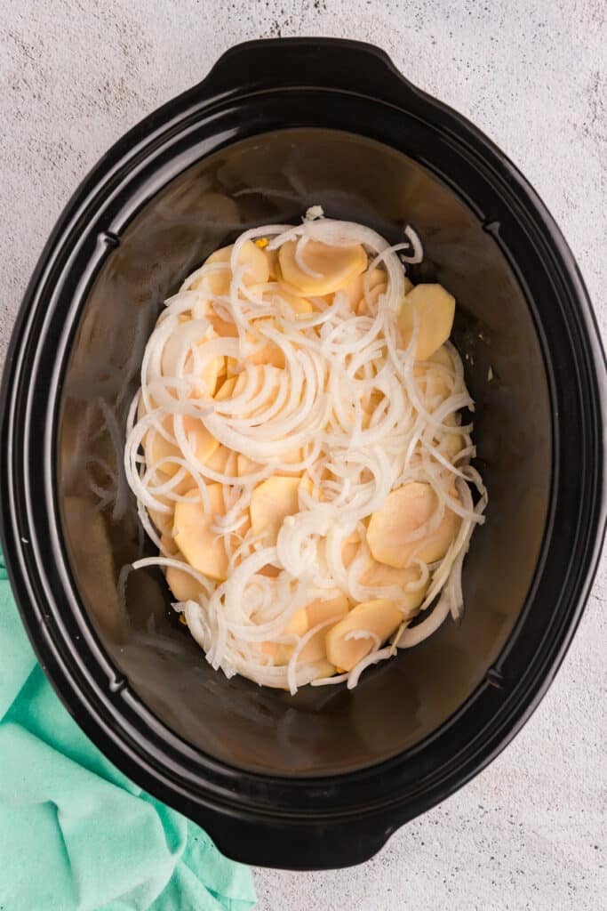 Sliced potatoes and onions layered in a crockpot.