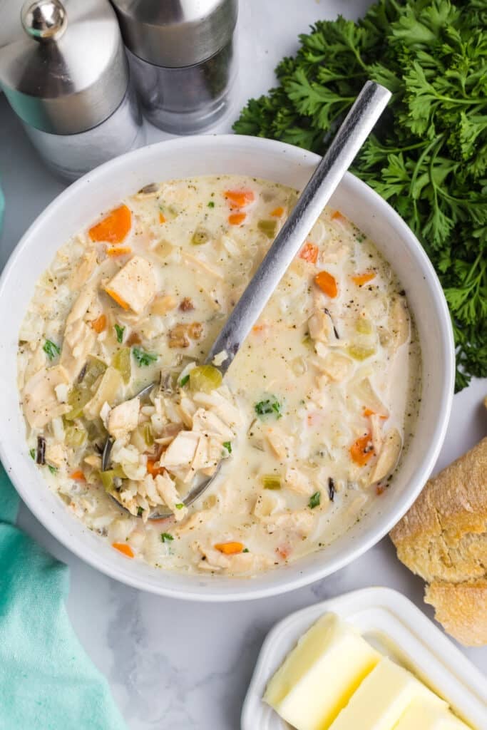 A bowl of creamy turkey rice soup with vegetables with a spoon in it.