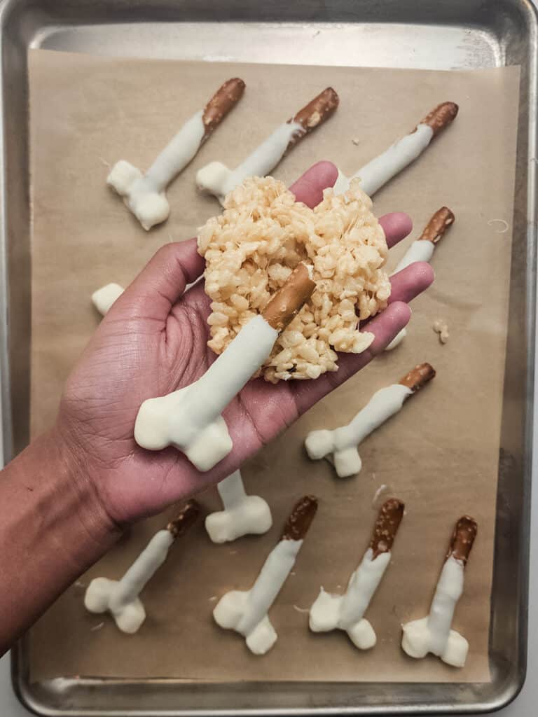 a hand wrapping rice krispie treats around a pretzel rod to look like a turkey leg.