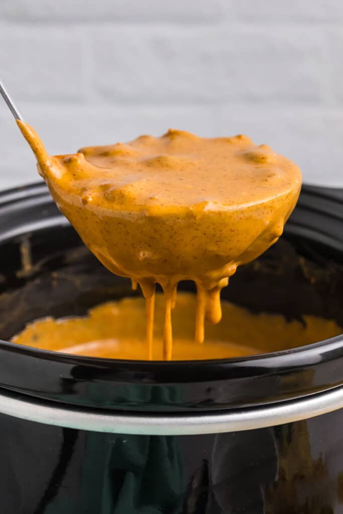 A ladle of creamy queso being lifted from a black crockpot.