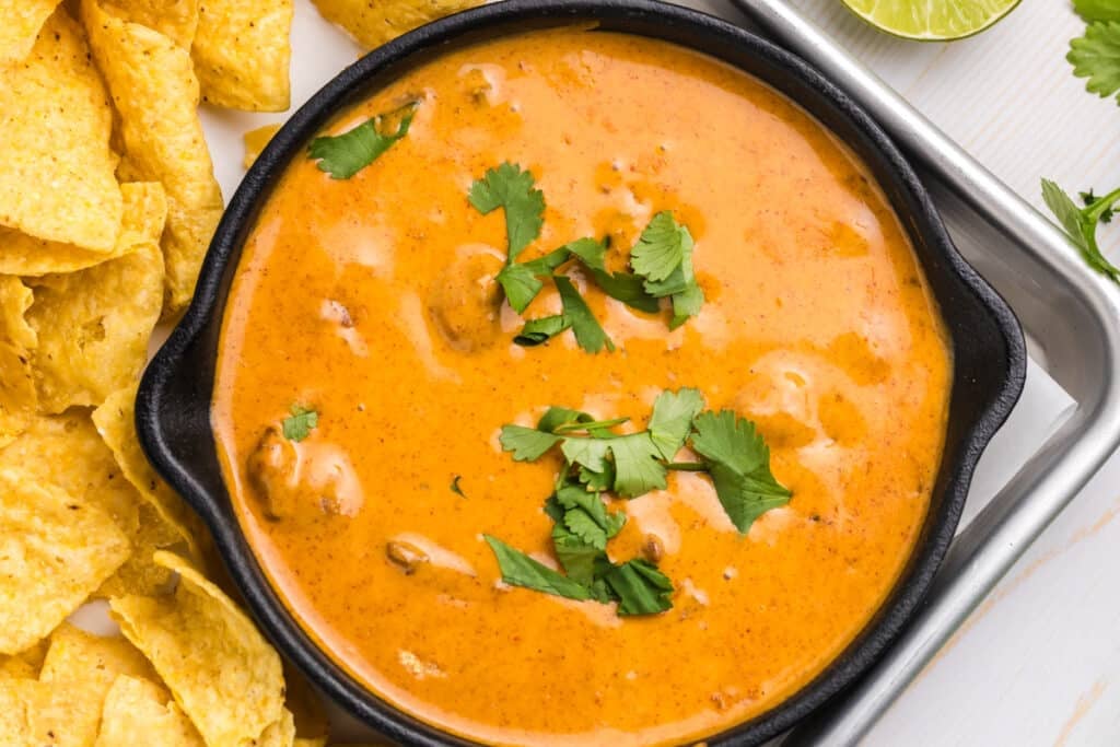 A skillet of queso dip topped with fresh cilantro and surrounded by tortilla chips.
