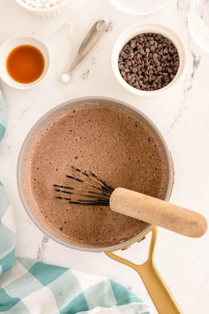 A saucepan of whisked hot chocolate with a wooden whisk.