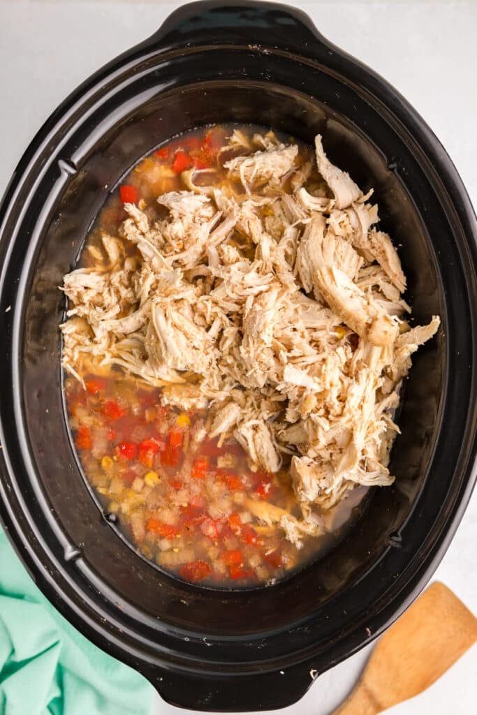 shredded chicken going into a slow cooker of tortilla soup.