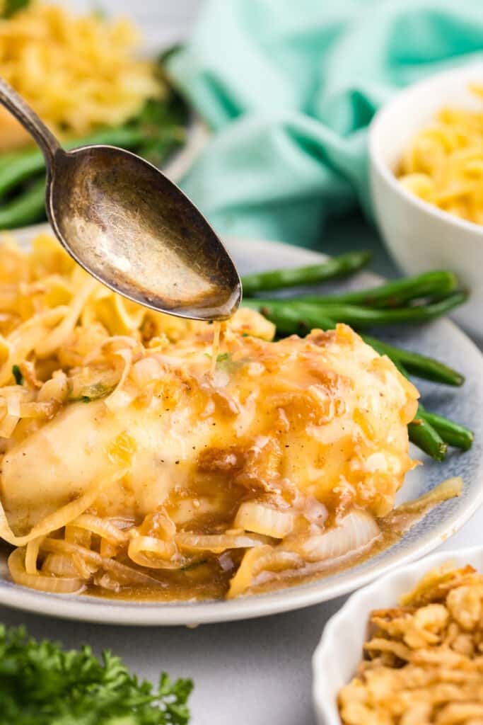 Spoon drizzling sauce over French onion chicken.