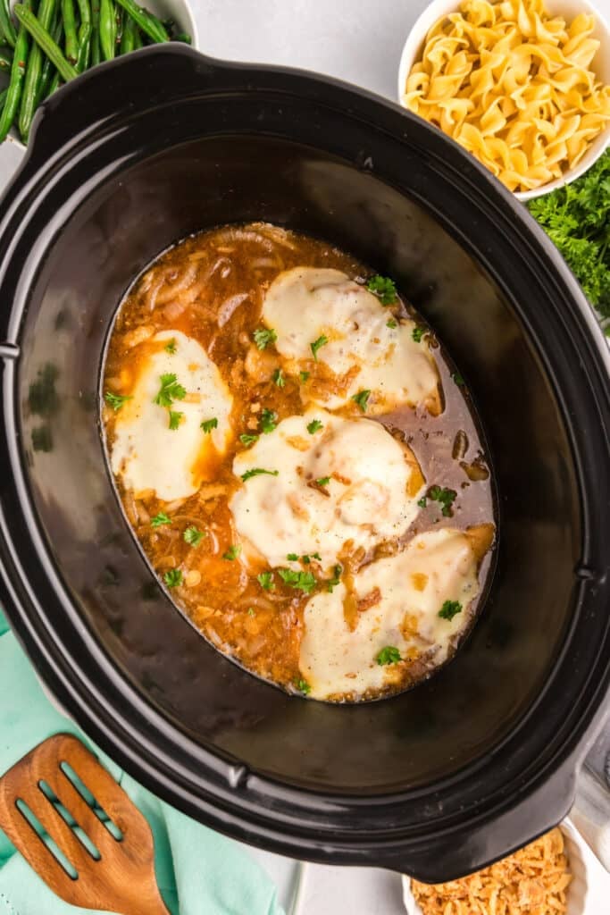 Melted cheese-covered chicken in a slow cooker, garnished with parsley.