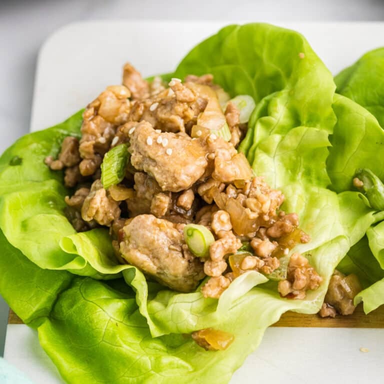 Chicken lettuce wrap with sesame seeds on a wooden board.