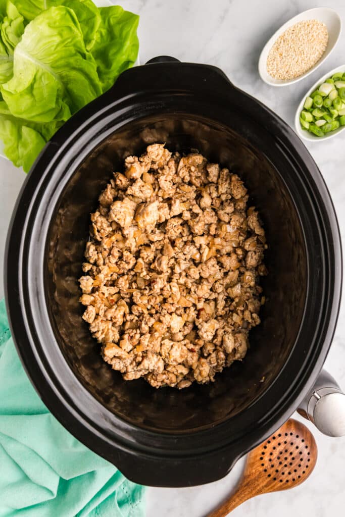 Cooked chicken mixture in a slow cooker with fresh toppings nearby.