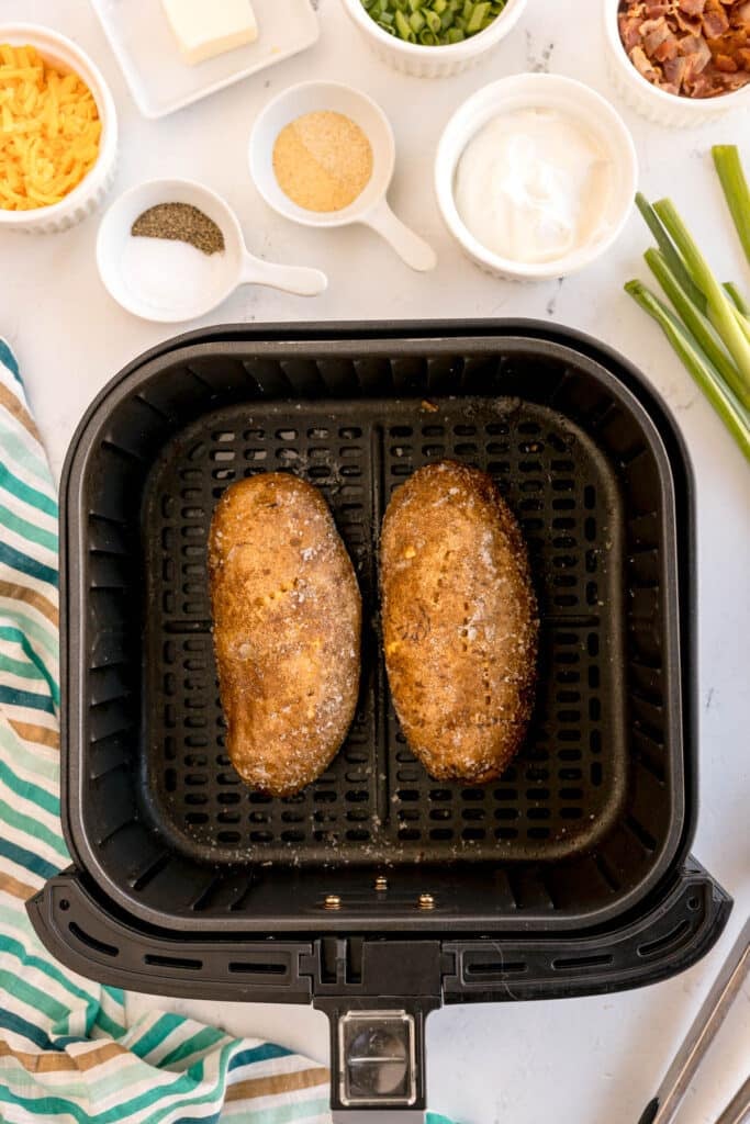 two russet potatoes in an air fryer basket.