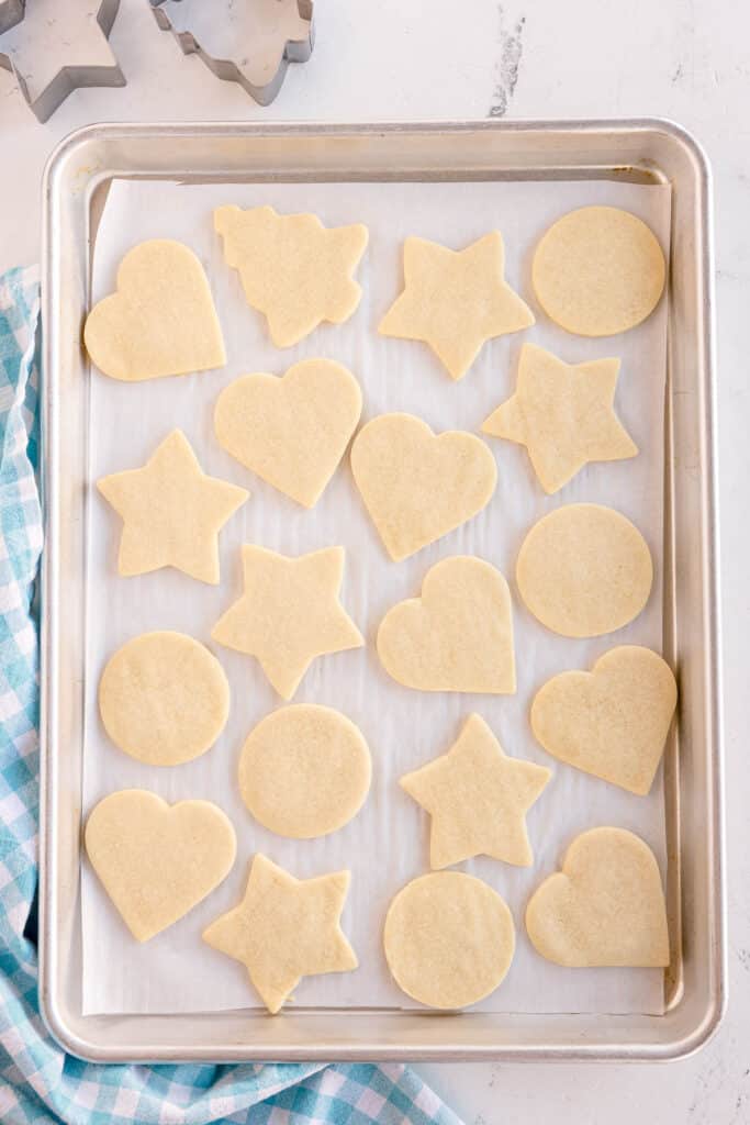 A tray of freshly baked sugar cookies, with heart, star, and circle shapes, sits cooling on parchment paper.