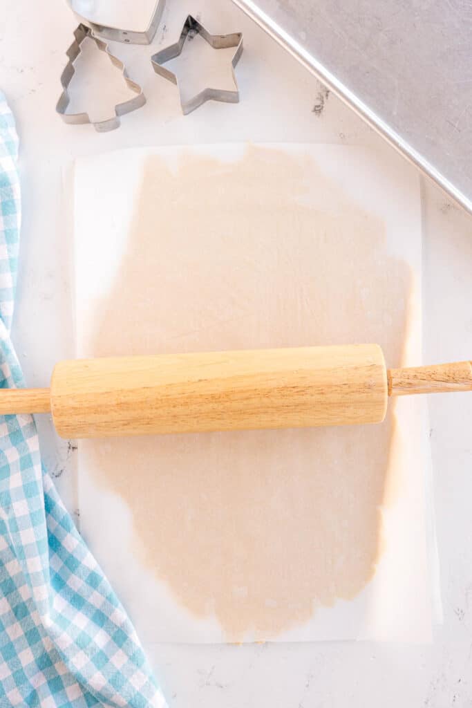 A rolling pin pressing cookie dough between parchment paper.