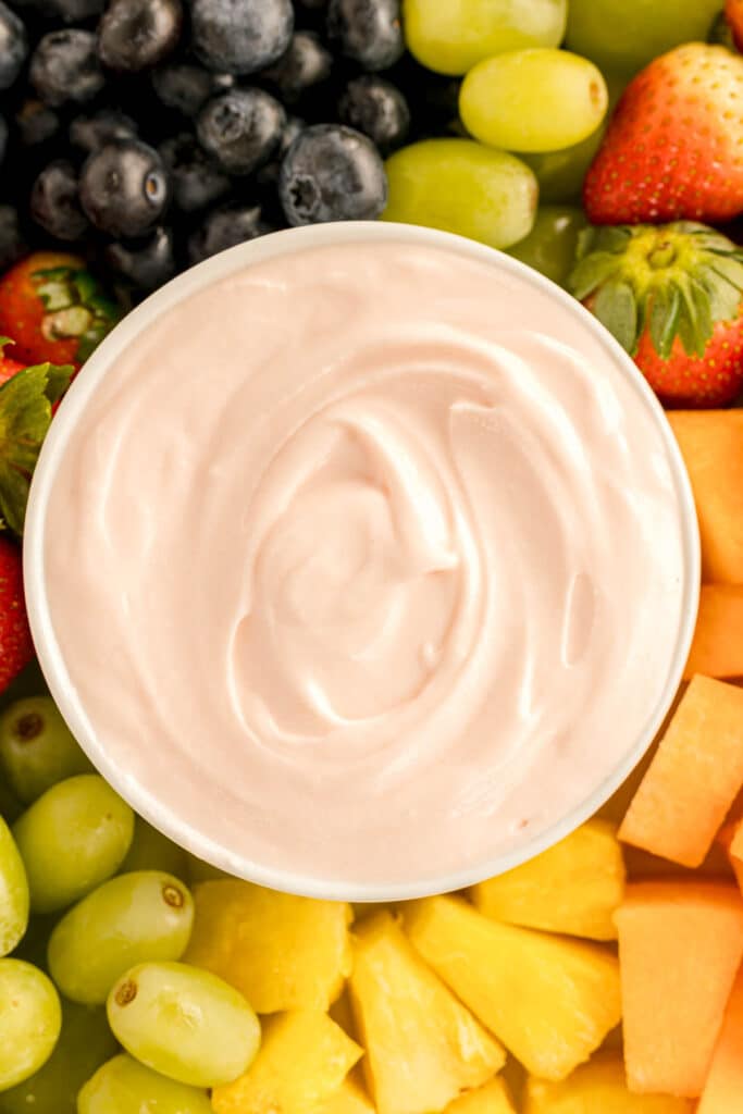 closeup overhead view of cream cheese fruit dip surrounded by cut fruit.