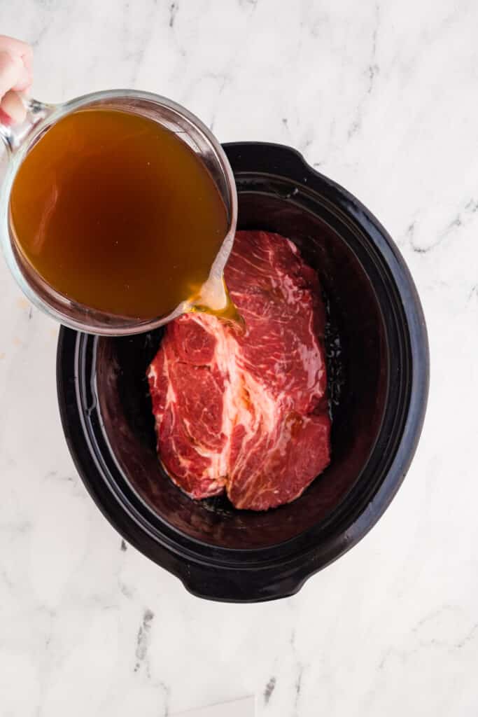 beef broth pouring over a roast in a slow cooker.