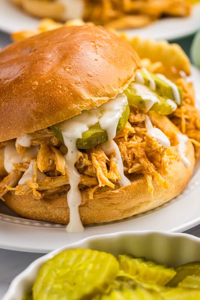 nashville hot chicken sandwich on a plate with pickles and ranch dressing.