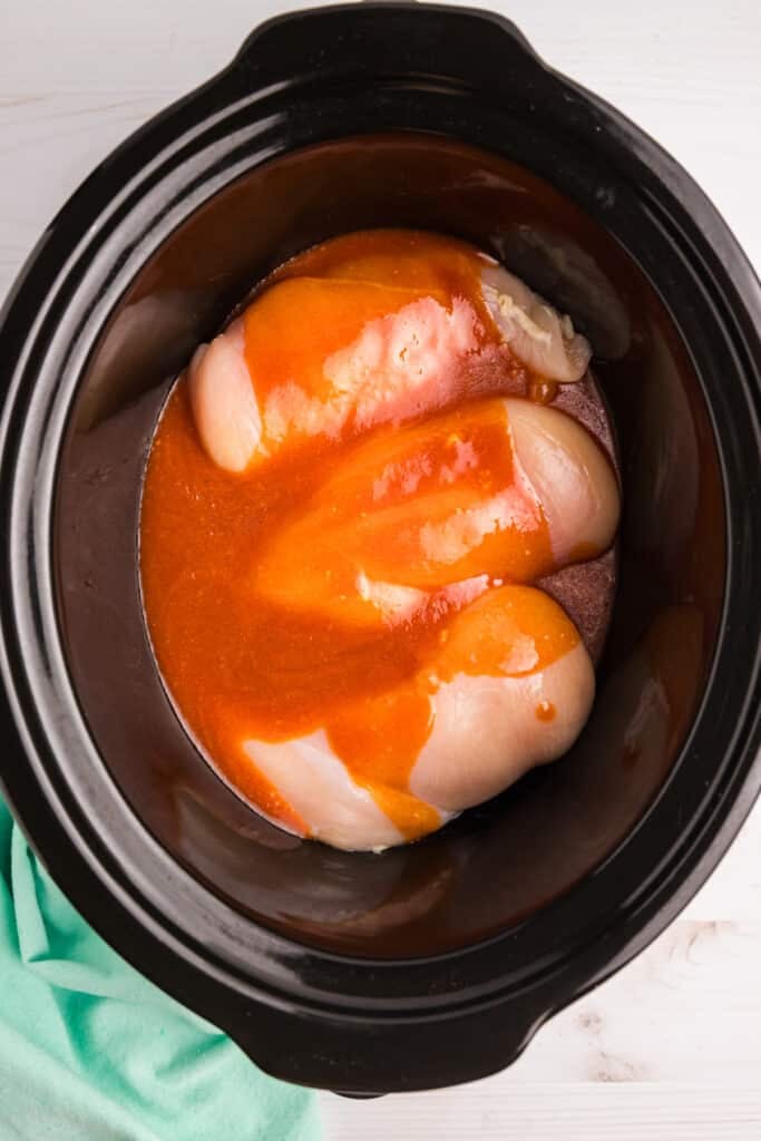 nashville hot sauce poured over raw chicken breasts in a crockpot.