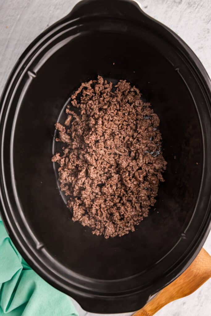 browned ground beef in the bottom of a slow cooker.