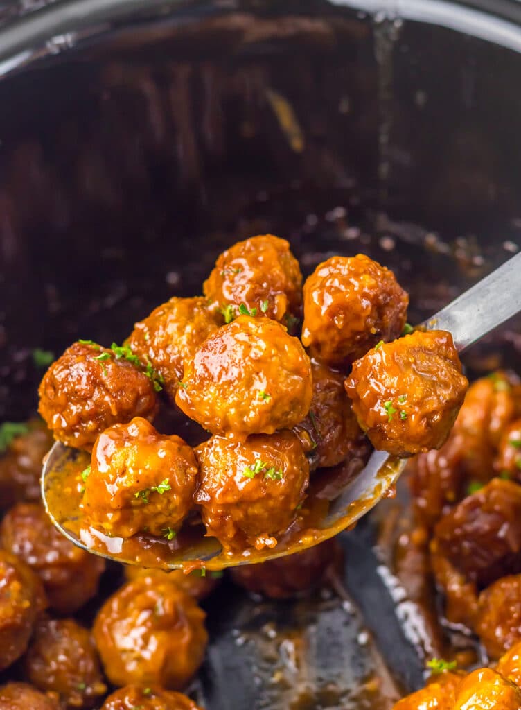 spoon lifting meatballs from a slow cooker.