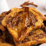 Close-up of stacked French toast with syrup on top and cinnamon sticks in the background.