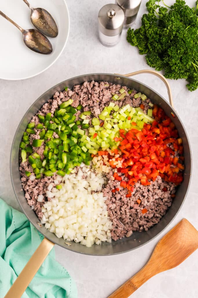 Chopped vegetables on top of cooked ground meat in a skillet.