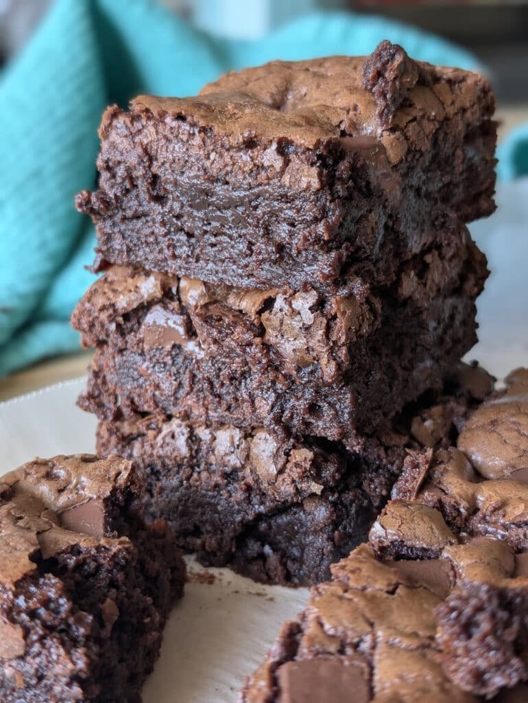 Stack of gooey brownies with shiny, crackly tops and melty chocolate chunks.