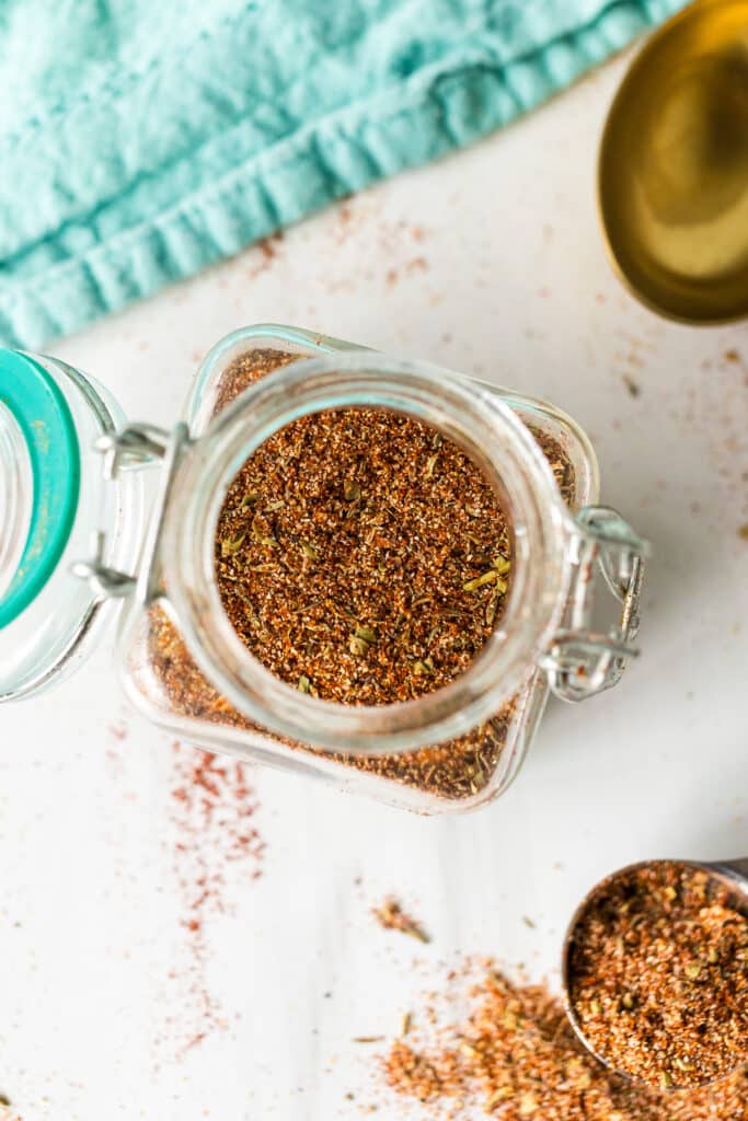 Top view of a glass jar filled with Cajun seasoning, with some spilled nearby