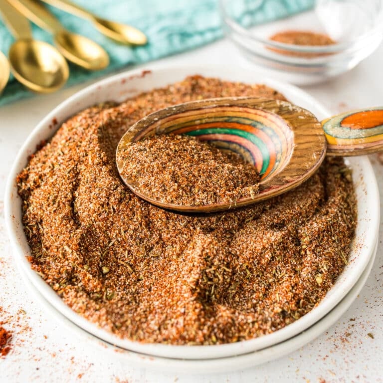 Wooden spoon scooping Cajun seasoning from a full white bowl.