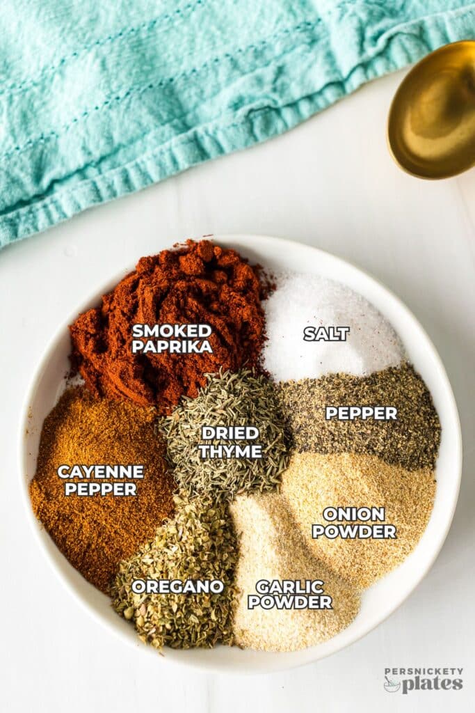 Bowl of labeled spices for Cajun seasoning, on a white surface.