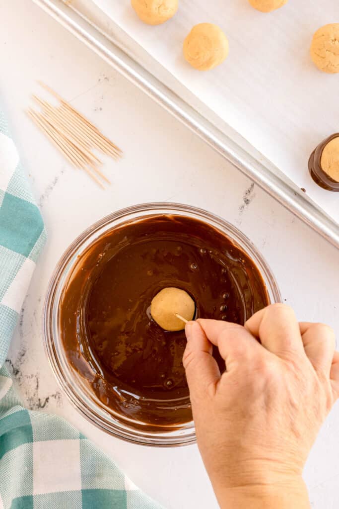 Dipping a peanut butter ball into chocolate with a toothpick.