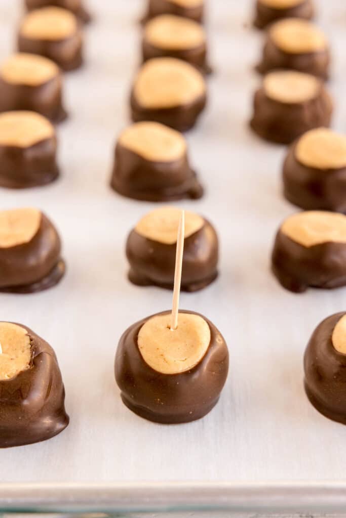Buckeye balls on parchment paper with toothpicks inserted.
