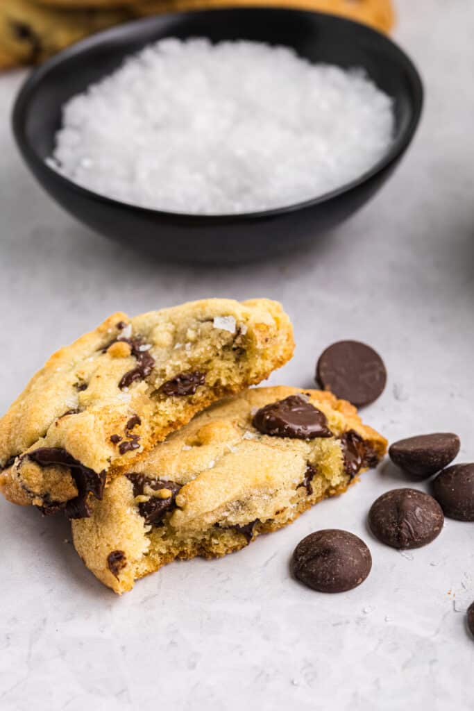 A stack of two soft chocolate chip cookies with melted chocolate chips and sea salt on a white surface.
