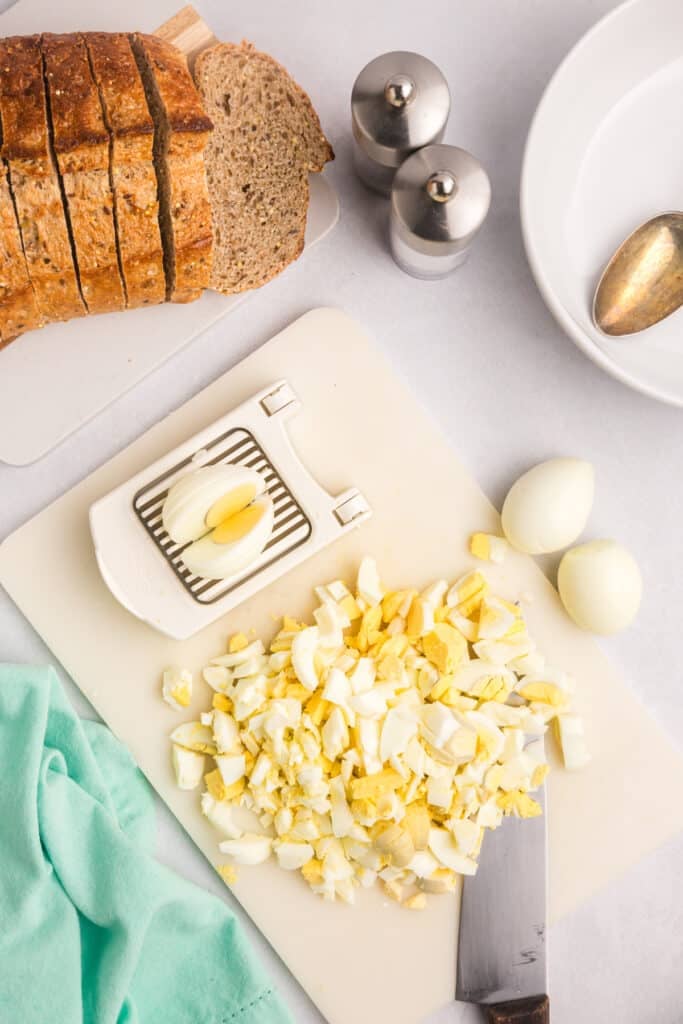 Chopped eggs on a cutting board with an egg slicer and bread.