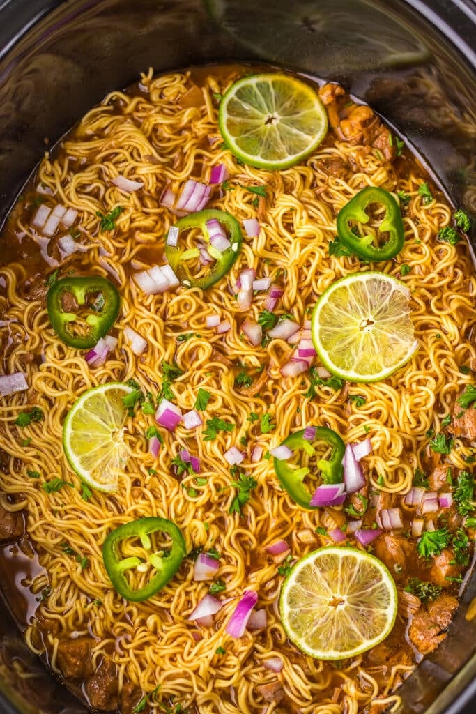 Birria ramen in a slow cooker with lime, jalapeƱo, and red onion.