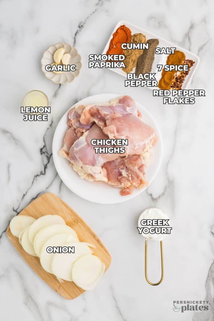 Flat lay of chicken shawarma ingredients including chicken thighs, spices, lemon juice, and yogurt.