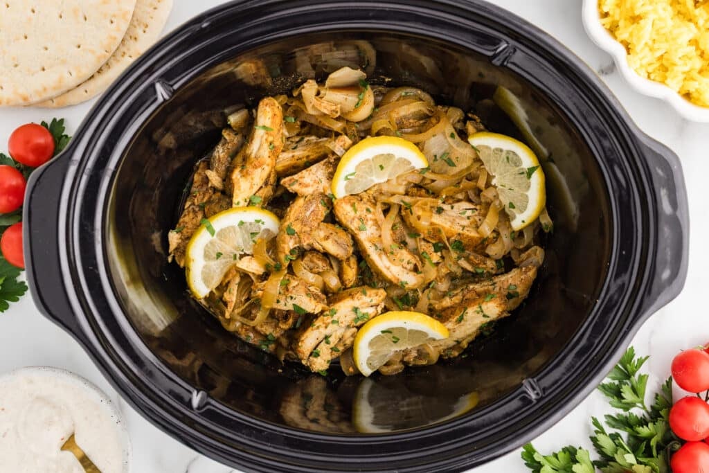 Cooked chicken shawarma with onions and lemon slices in a slow cooker.