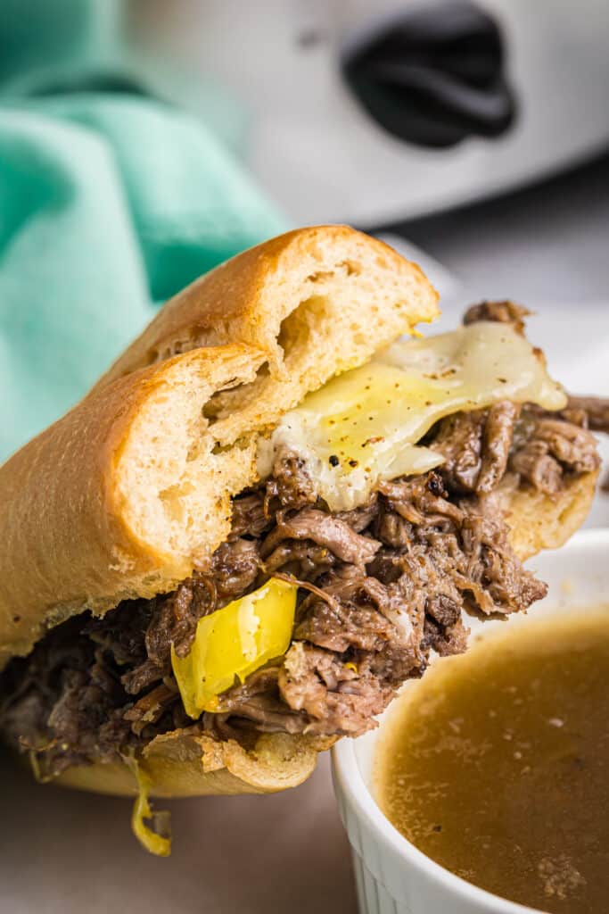 Italian beef sandwich with melted cheese and peppers next to a bowl of au jus.