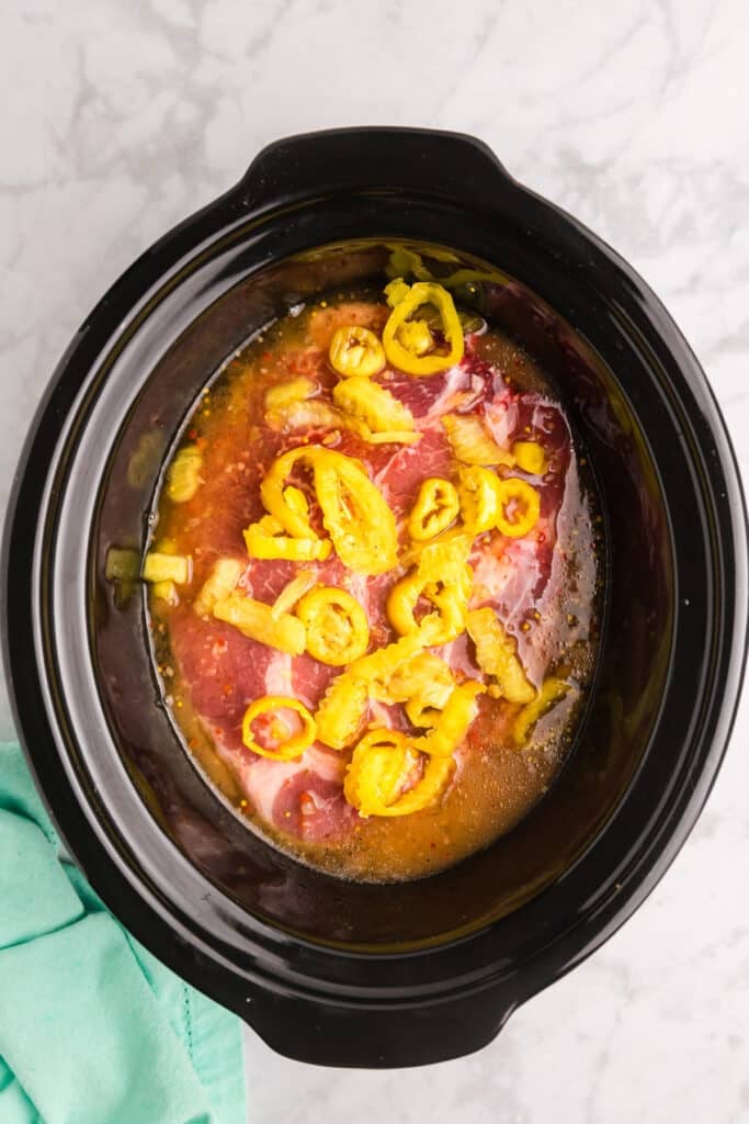 Top view of shredded beef with yellow peppers inside a black slow cooker.