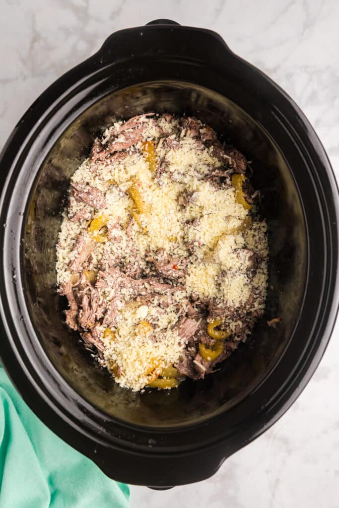 Shredded beef and yellow peppers in a crockpot topped with grated Parmesan cheese.