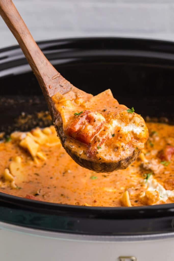 Wooden spoon lifting lasagna soup from a slow cooker.