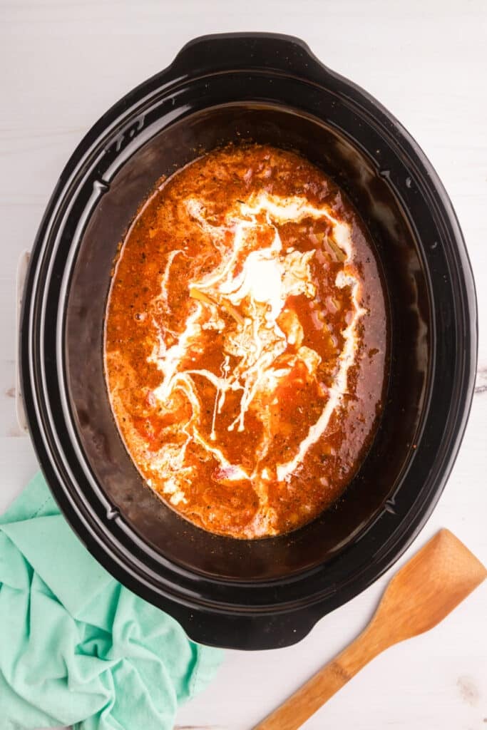 Cream being added to lasagna soup in a slow cooker.