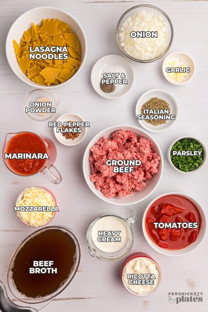Flat lay of labeled lasagna soup ingredients in bowls on a white surface.