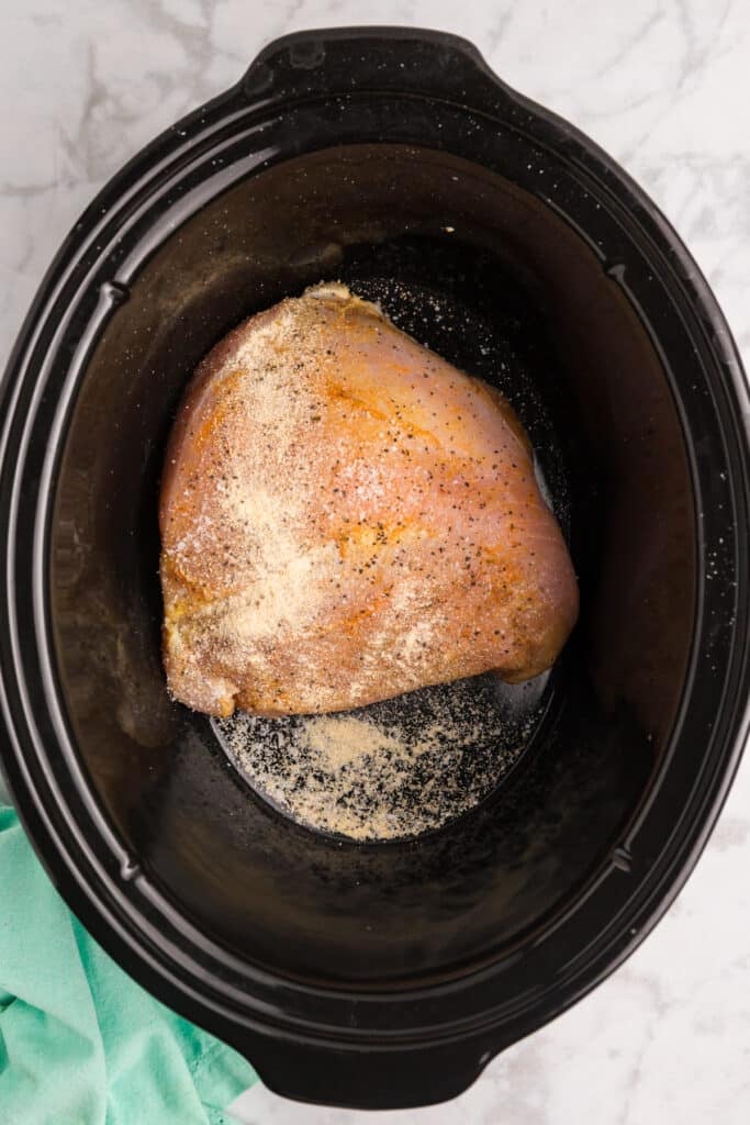 Seasoned raw turkey breast inside a slow cooker.