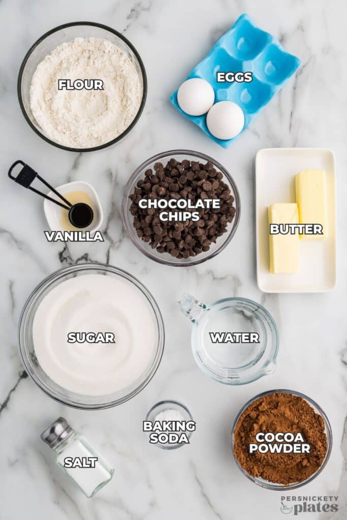 Labeled brownie ingredients in bowls on a white marble surface.