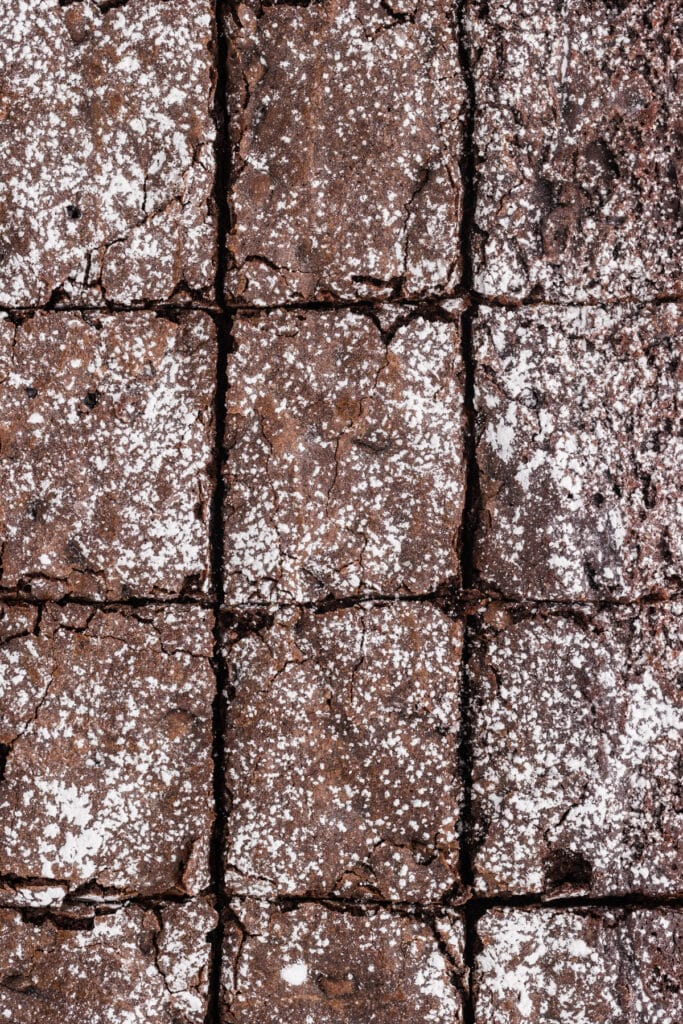 A full pan of chocolate brownies cut into squares, all topped with a light dusting of powdered sugar.
