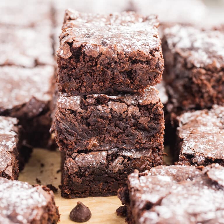 Square image of stacked brownies surrounded by more brownie pieces.