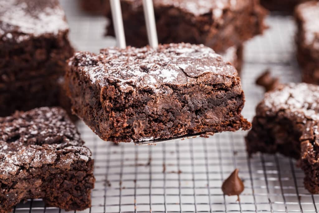 Fudgy brownie square on a metal spatula with more brownies in the background.