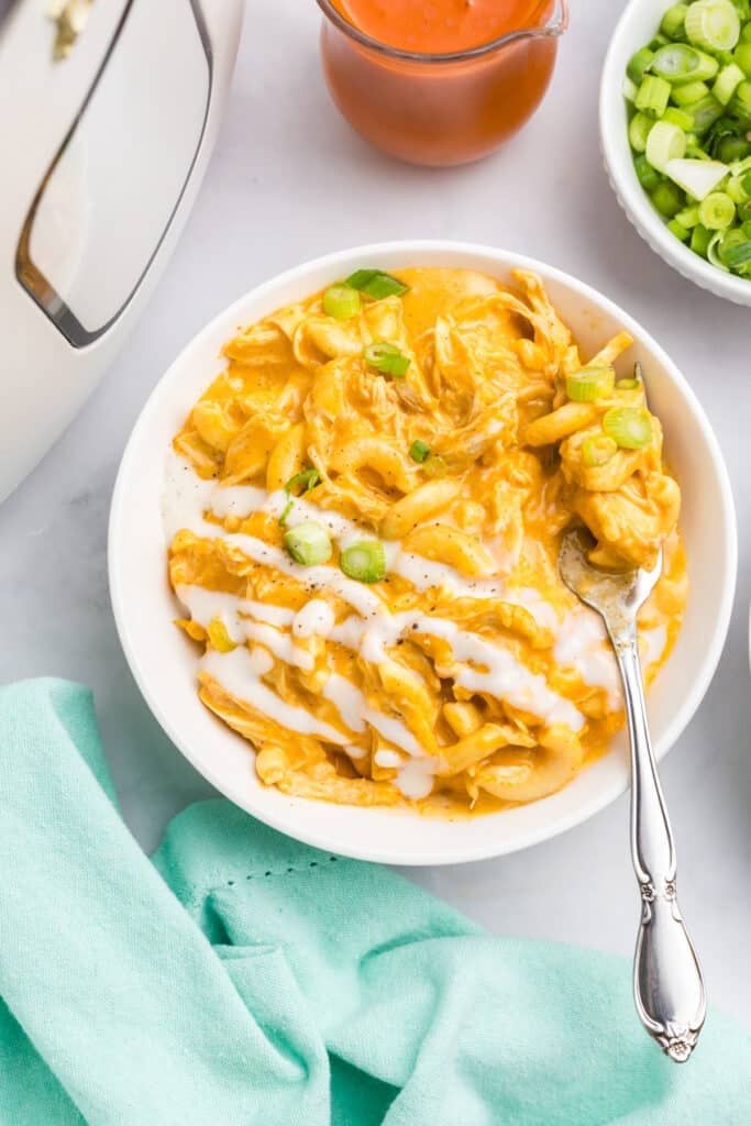 Buffalo chicken mac and cheese in a white bowl topped with ranch and green onions.