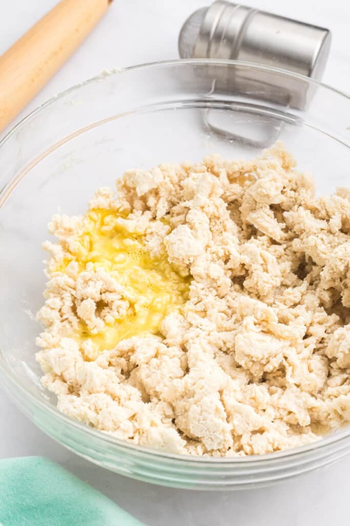 Partially mixed pie dough with a cracked egg in a glass bowl.