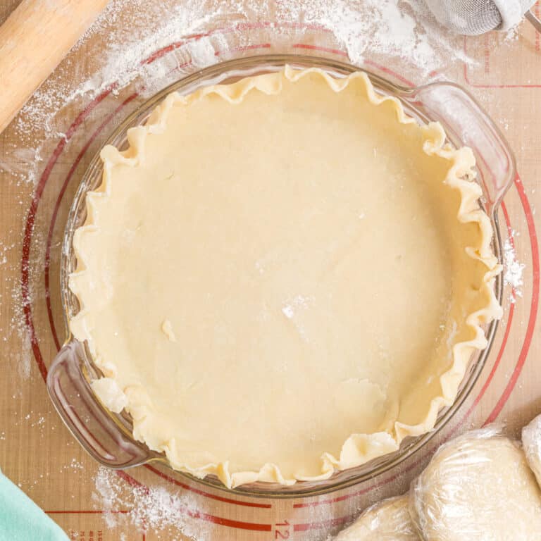 Unbaked pie crust in a dish with wrapped dough discs beside it.