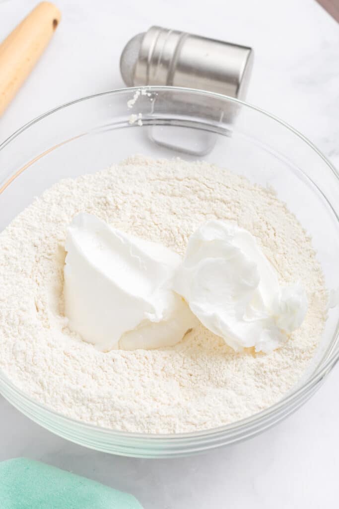 Two scoops of shortening on top of flour in a mixing bowl.
